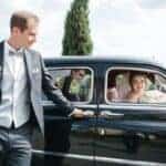 Groom opening car door for bride in vintage car