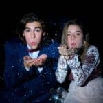 Young couple blowing glitter at camera with disco ball