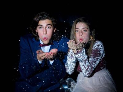 Young couple blowing glitter at camera with disco ball