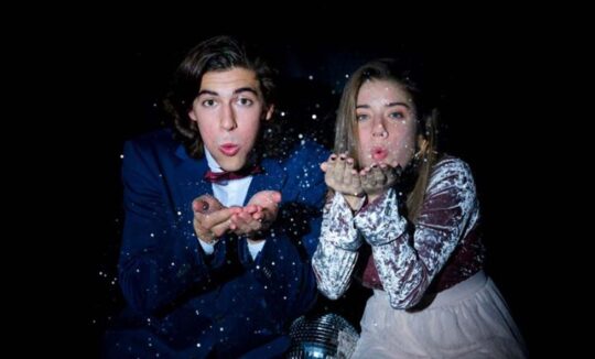 Young couple blowing glitter at camera with disco ball
