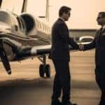 Two businessmen shaking hands beside private airplane