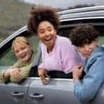 Three friends leaning out of car windows smiling