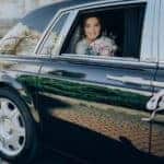 Bride smiling in decorated wedding car holding bouquet