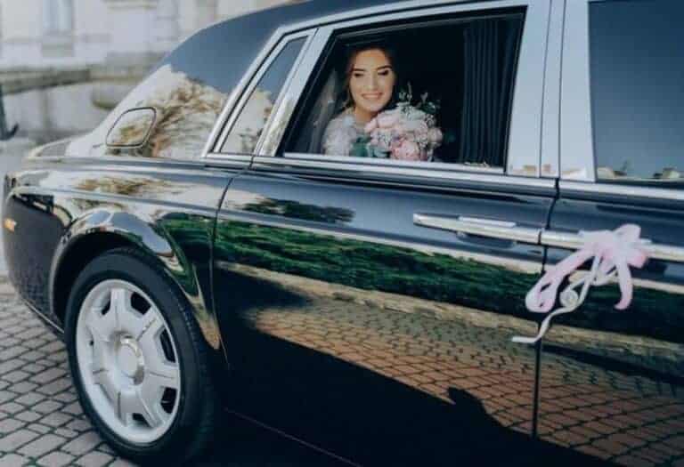 Bride smiling in decorated wedding car holding bouquet