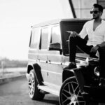 Man sitting on black SUV wearing sunglasses