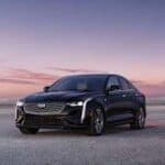 Black luxury sedan parked by ocean at sunset