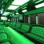 Green-lit luxury party bus interior with bench seating