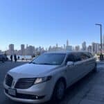 White stretch limousine parked by city skyline waterfront