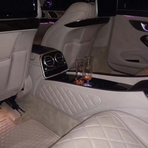 Luxurious car interior with quilted seats and two drinks.