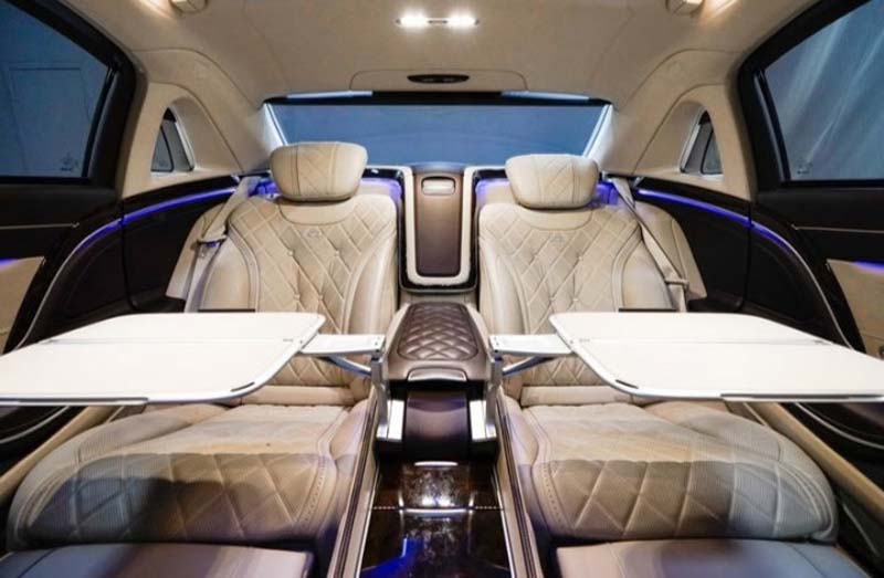 Luxurious car interior with quilted beige seats and deployable tables.