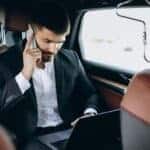 Businessman using laptop and phone in car
