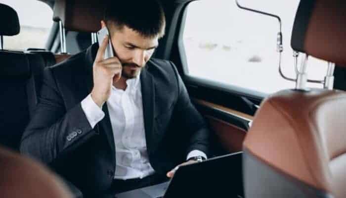Businessman using laptop and phone in car