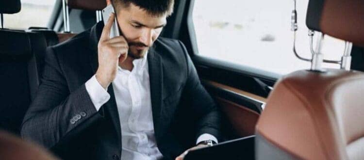 Businessman using laptop and phone in car