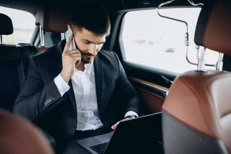 Businessman using laptop and phone in car