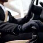 Man in suit driving car wearing black gloves