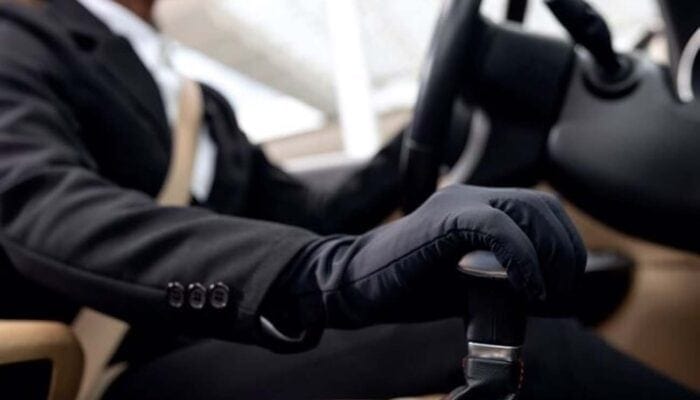 Man in suit driving car wearing black gloves