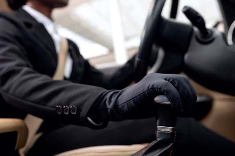 Man in suit driving car wearing black gloves