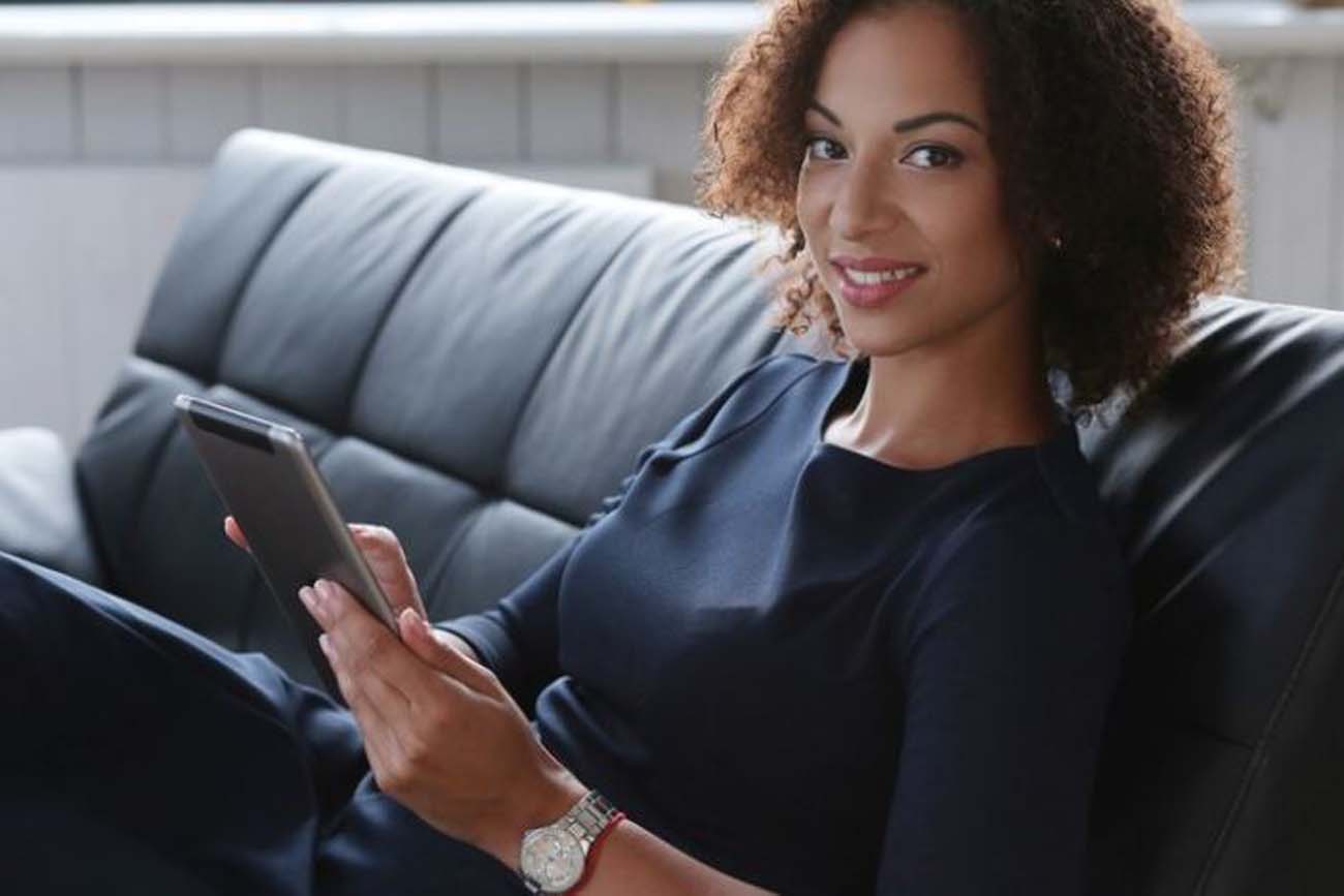 Woman sitting on couch holding tablet and smiling