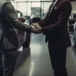 Two men shaking hands in car dealership showroom