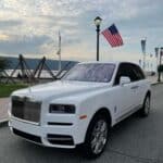 White Rolls-Royce parked by waterfront with American flag