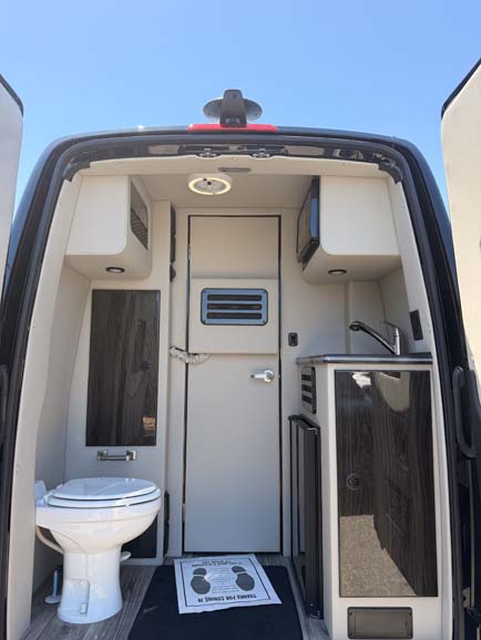 Interior view of a camper van with toilet and kitchenette.