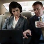 Two business professionals reviewing laptop in car backseat