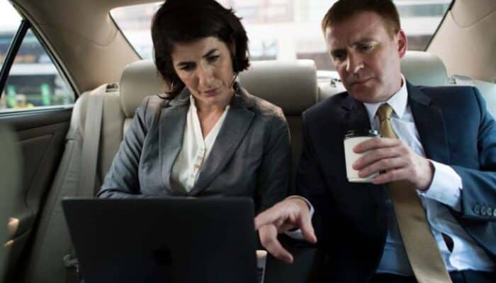 Two business professionals reviewing laptop in car backseat