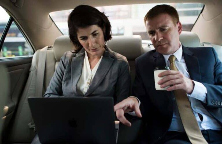 Two business professionals reviewing laptop in car backseat