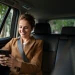 Woman smiling at smartphone in backseat of car