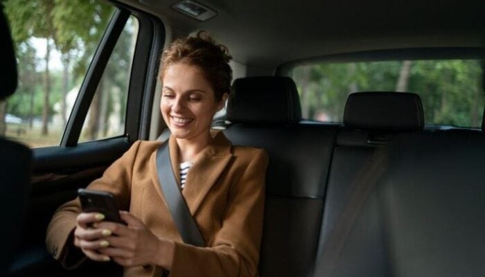Woman smiling at smartphone in backseat of car