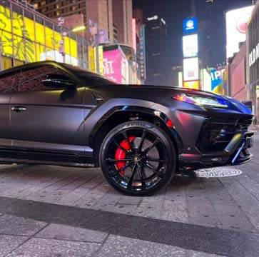 Matte black Lamborghini SUV in neon-lit city at night