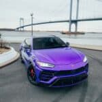 Purple Lamborghini SUV by suspension bridge waterfront