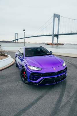 Purple Lamborghini SUV by suspension bridge waterfront