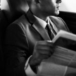 Man in suit reading newspaper in car