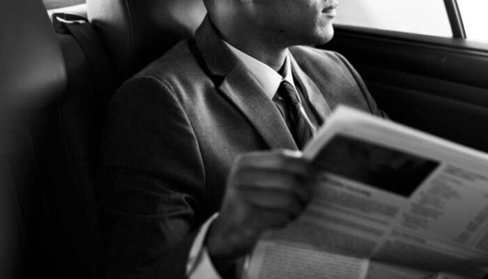 Man in suit reading newspaper in car