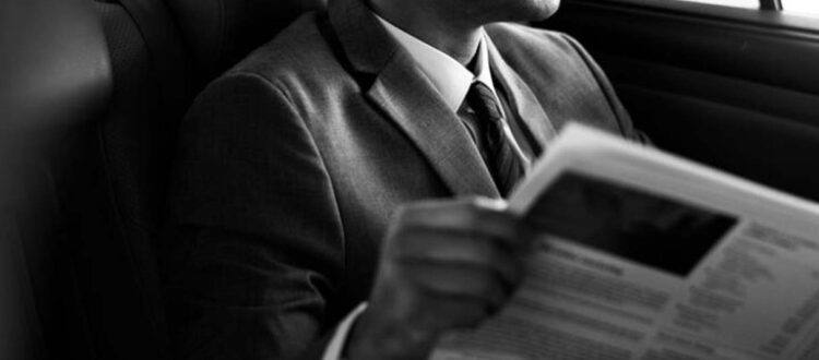 Man in suit reading newspaper in car