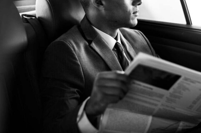 Man in suit reading newspaper in car