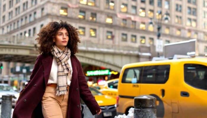 Woman walking in city street near yellow taxi