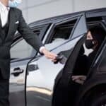 Chauffeur opening car door for masked female passenger