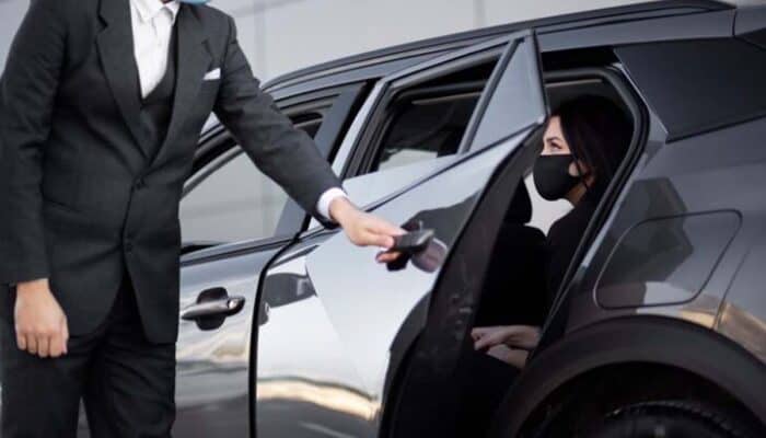 Chauffeur opening car door for masked female passenger