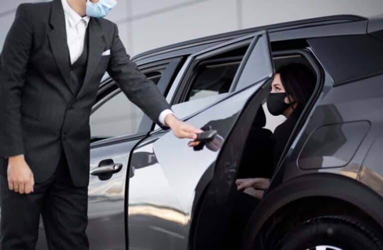 Chauffeur opening car door for masked female passenger