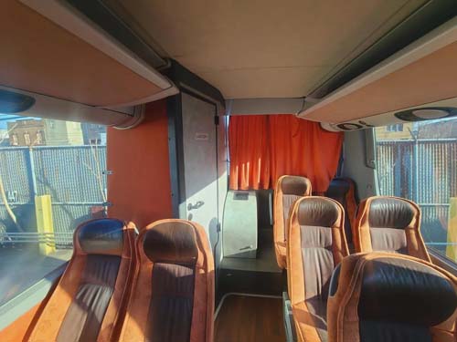 Empty coach bus interior with brown seats and orange curtain