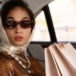 Woman wearing sunglasses and headscarf holding shopping bags in car