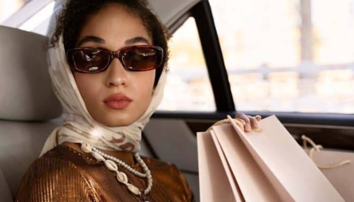Woman wearing sunglasses and headscarf holding shopping bags in car