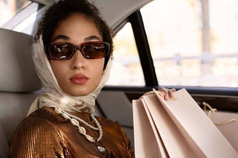 Woman wearing sunglasses and headscarf holding shopping bags in car