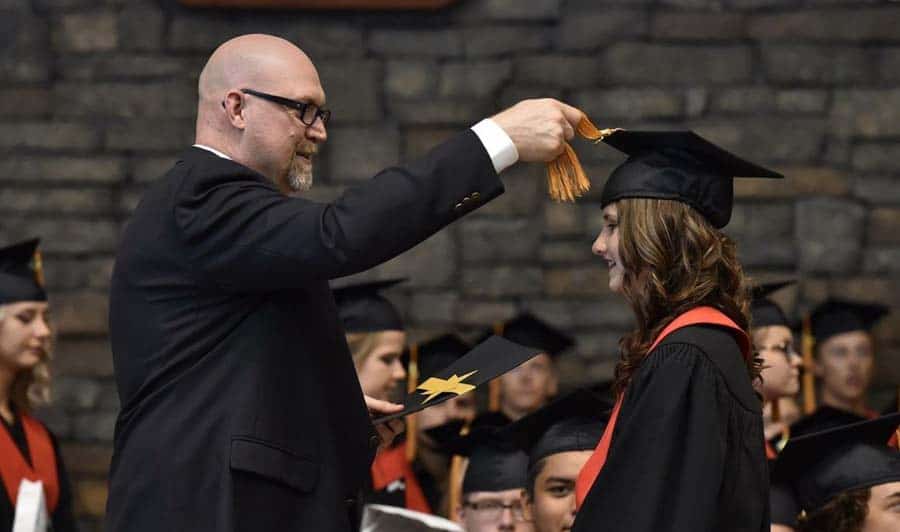 Man moving tassel on graduate during ceremony