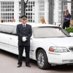 Chauffeur standing beside white limousine outside building