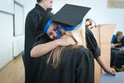 Two graduates in caps and gowns hugging