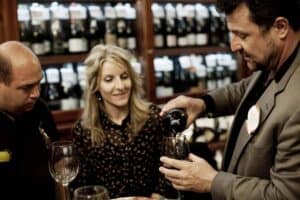 Man pouring red wine for couple in wine shop