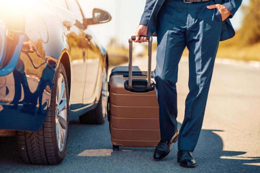 Businessman walking with rolling suitcase beside parked car